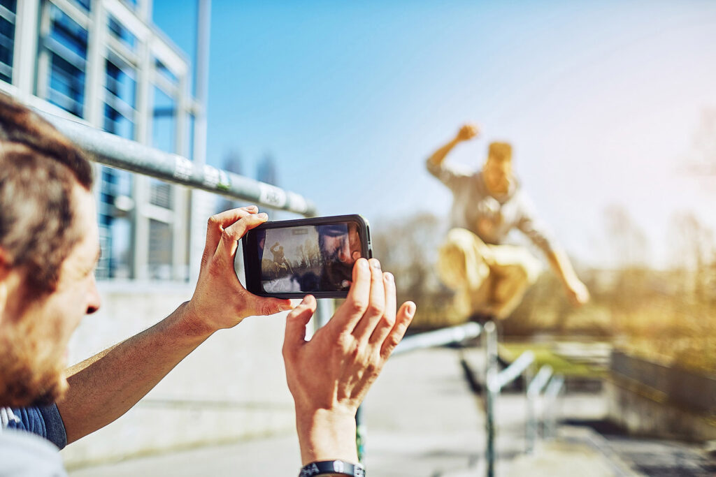 Streetrunning-Aufnahme eines jungen Mannes beim Filmen eines sportlichen Sprungs mit dem Smartphone – authentische Lifestyle-Werbung von Atelier Schulte in urbaner Umgebung.