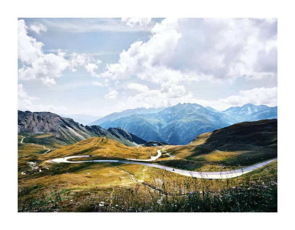 Hochalpenstraße im goldenen Licht, geschwungene Kurven vor Bergpanorama – Landschaftsfotografie Österreich von Atelier Schulte