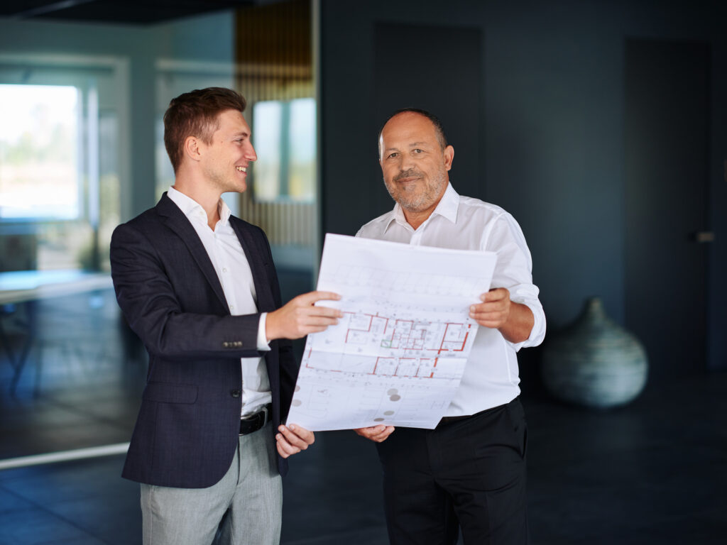 Businessportrait Konzepthaus – Architekten bei Teamwork mit Bauplänen, aufgenommen von Atelier Schulte