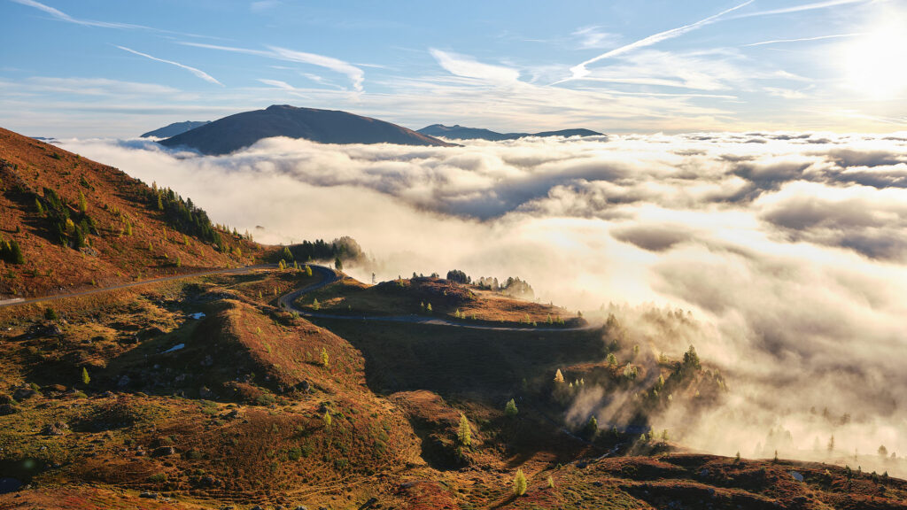 Blick über die Nockalmstraße im Morgenlicht mit Nebelmeer und Alpengipfeln – stimmungsvolle Landschaftsfotografie von Fotograf Florian Schulte, Atelier Schulte, österreichweit und über die Grenzen hinaus.
