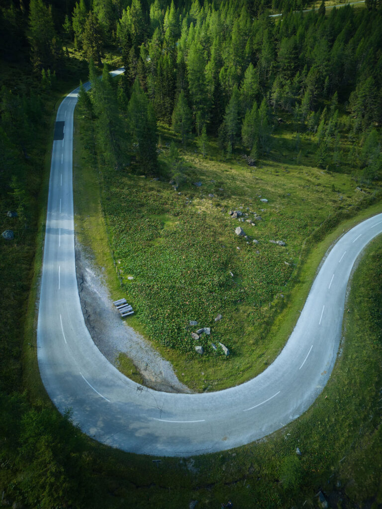 Drohnenaufnahme einer geschwungenen Kurve der Nockalmstraße durch dichte Wälder – moderne Landschaftsfotografie von Atelier Schulte, Fotograf Florian Schulte, österreichweit und über die Grenzen hinaus.