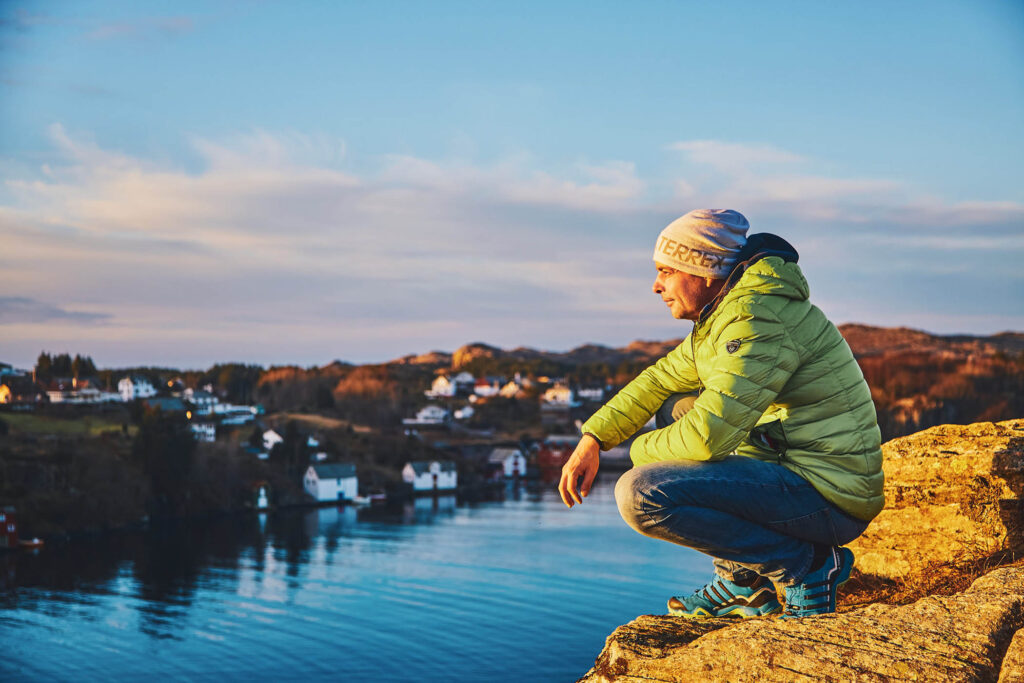 Person in Outdoorbekleidung beobachtet den Sonnenaufgang über einer fjordähnlichen Küstenlandschaft – alpine Atmosphäre und professionelle Outdoor-Fotografie von Atelier Schulte