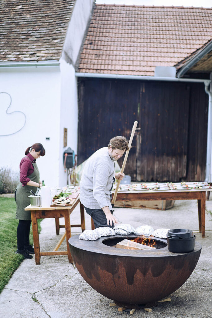 Reportagefotografie von Atelier Schulte – Kochteam bei der Zubereitung regionaler Speisen über offenem Feuer im Innenhof am Wagram in Niederösterreich. Authentische Kulinarikreportage mit Atmosphäre und Handwerk.