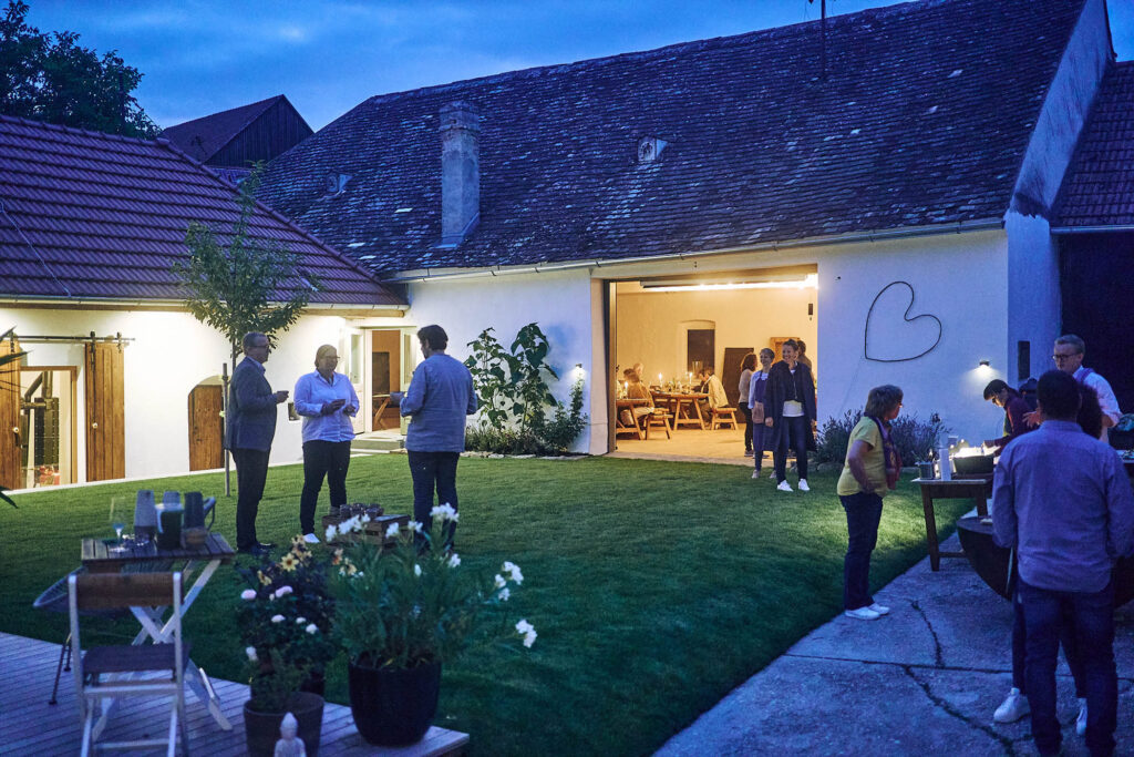 Abendliche Stimmung im Innenhof mit Gästen und Kerzenlicht bei Essen vor Ort am Wagram in Niederösterreich. Atmosphärische Eventfotografie, Atelier Schulte.