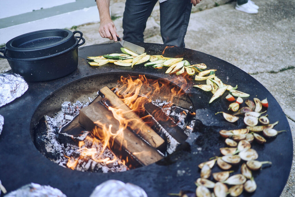 Zucchini und Gemüse werden auf offener Feuerstelle zubereitet bei Essen vor Ort am Wagram. Authentische Foodfotografie mit Feuer und Handwerk, fotografiert von Atelier Schulte.