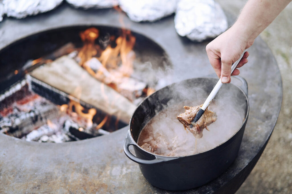 Kochtopf über offenem Feuer mit dampfendem Fleisch bei Essen vor Ort am Wagram in Niederösterreich. Authentische Foodfotografie mit Wärme, Handwerk und Atmosphäre, fotografiert von Atelier Schulte.