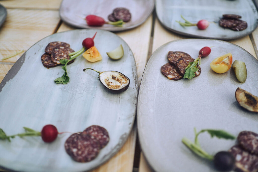 Detailaufnahme angerichteter Vorspeisenteller mit Wurst, Gemüse und Radieschen bei Essen vor Ort am Wagram in Niederösterreich. Authentische Foodfotografie mit Fokus auf regionale Zutaten, Atelier Schulte.