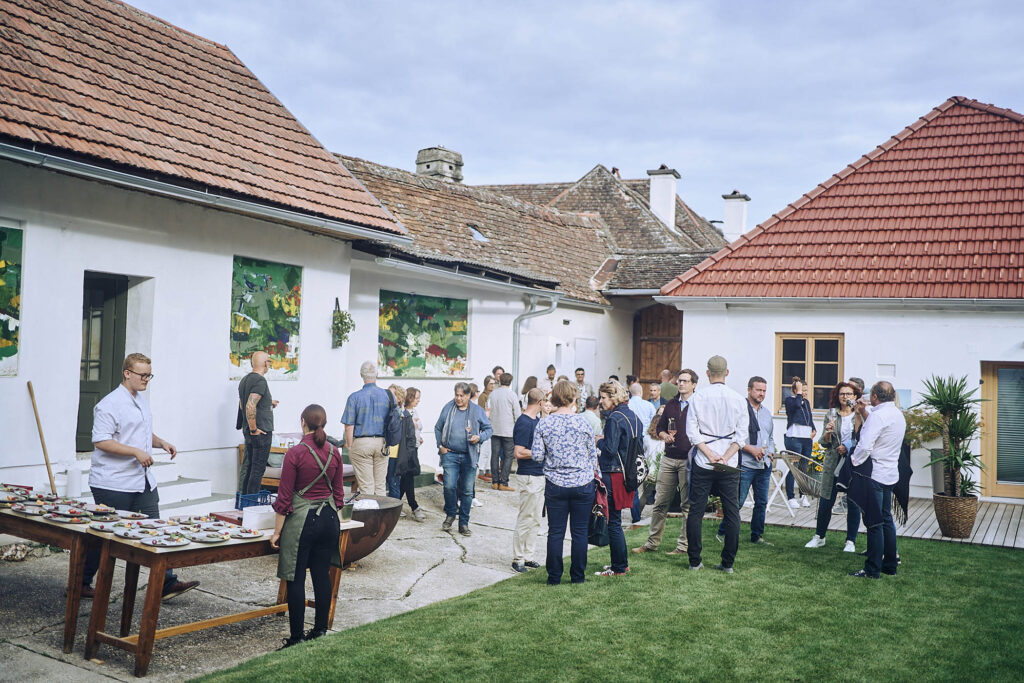 Gäste versammeln sich im Innenhof beim Kulinarikevent Essen vor Ort am Wagram in Niederösterreich. Authentische Reportagefotografie mit natürlicher Lichtstimmung, Atelier Schulte.