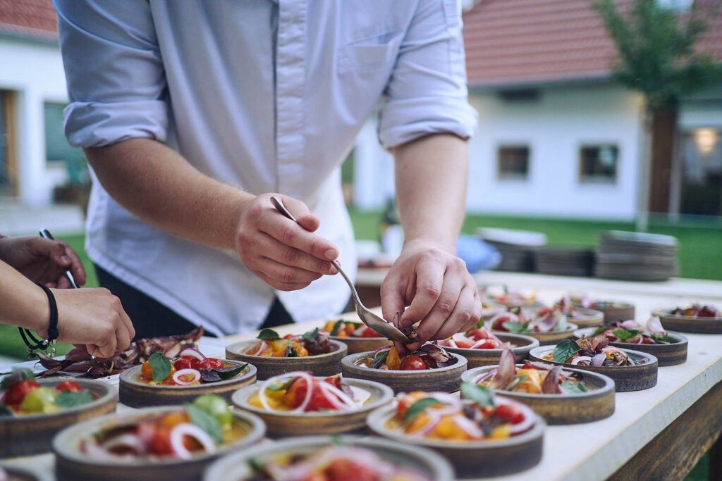 Koch richtet bunte Teller mit Gemüse und Kräutern an bei Essen vor Ort am Wagram in Niederösterreich. Kulinarische Reportagefotografie, Atelier Schulte.
