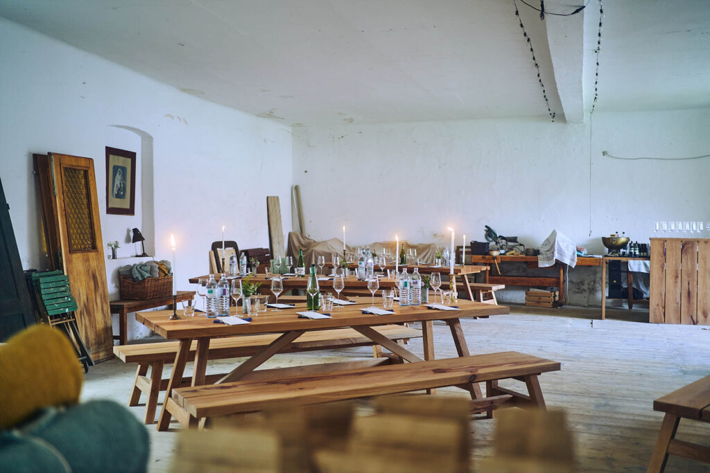 Festlich gedeckte Holztische mit Kerzenlicht im Innenraum von Essen vor Ort am Wagram in Niederösterreich. Stimmungsvolle Kulinarikreportage mit warmem Licht und Atmosphäre, Atelier Schulte.