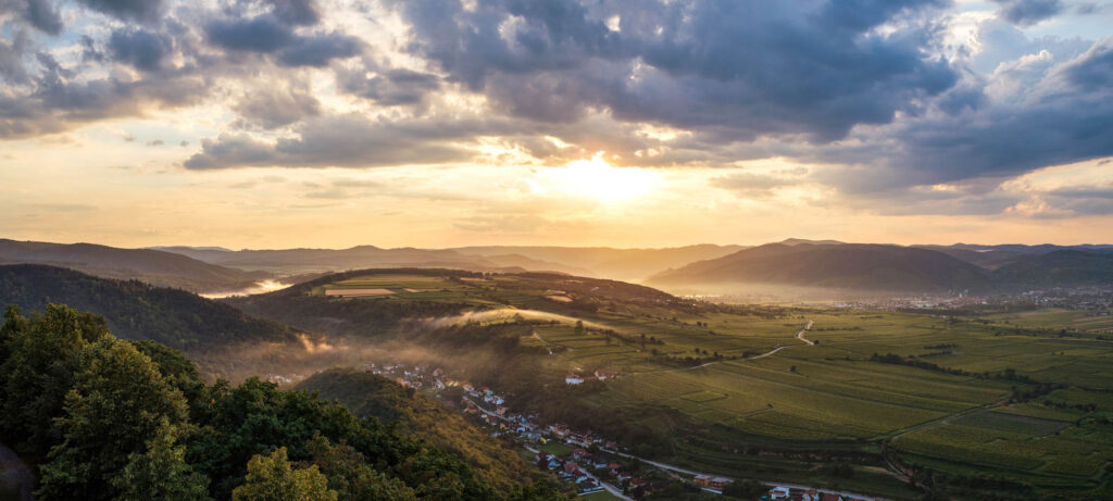 Sonnenuntergang über den Hügeln und Weinlandschaften nahe Göttweig, goldene Lichtstimmung mit Nebelschwaden im Tal – professionelle Landschaftsfotografie von Atelier Schulte