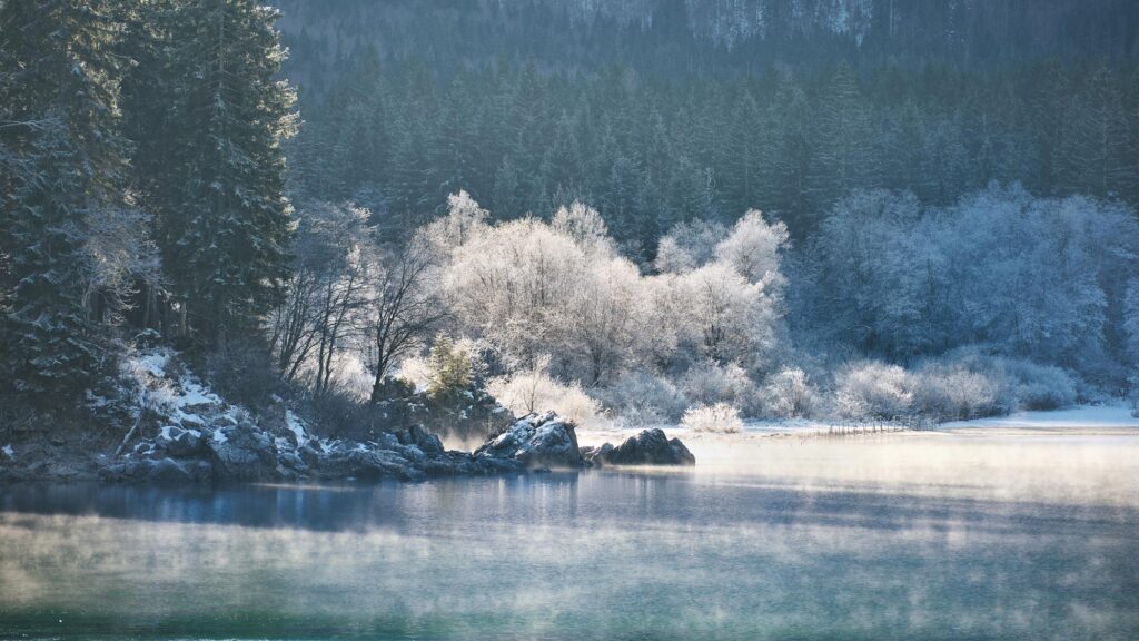 Winterlicher Sonnenaufgang am Lago di Fusine in Italien mit ruhigem See, Nebel und frostigen Bäumen – Landschaftsfotografie von Atelier Schulte