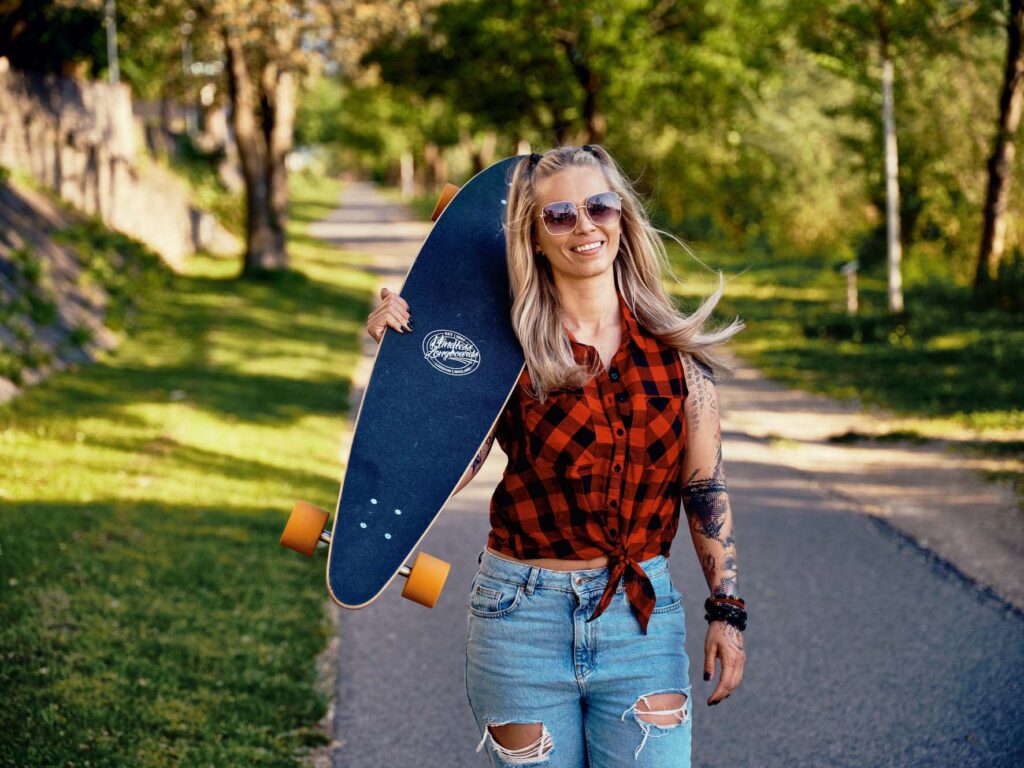 Lifestyle-Outdoor-Fotografie in Villach, Kärnten: junge Frau mit Skateboard auf grünem Naturweg, sommerliche Stimmung, natürliches Licht und entspannter Lifestyle