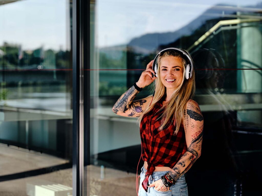 Lifestyle-Outdoor-Fotografie in Villach, Kärnten: urbanes Portrait einer jungen Frau mit Kopfhörern vor moderner Glasfassade, natürliches Licht und entspannte Stimmung