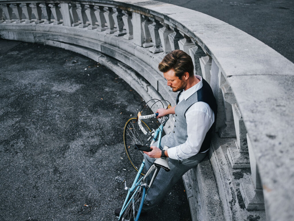 Mann mit Fahrrad lehnt an Balustrade im Wiener Stadtraum – urbaner Lifestyle-Moment zwischen Bewegung und Pause