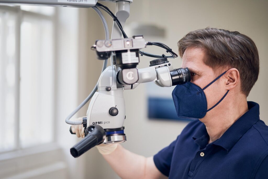 Zahnarzt bei präziser Behandlung mit Operationsmikroskop in moderner Zahnarztpraxis in Wien.