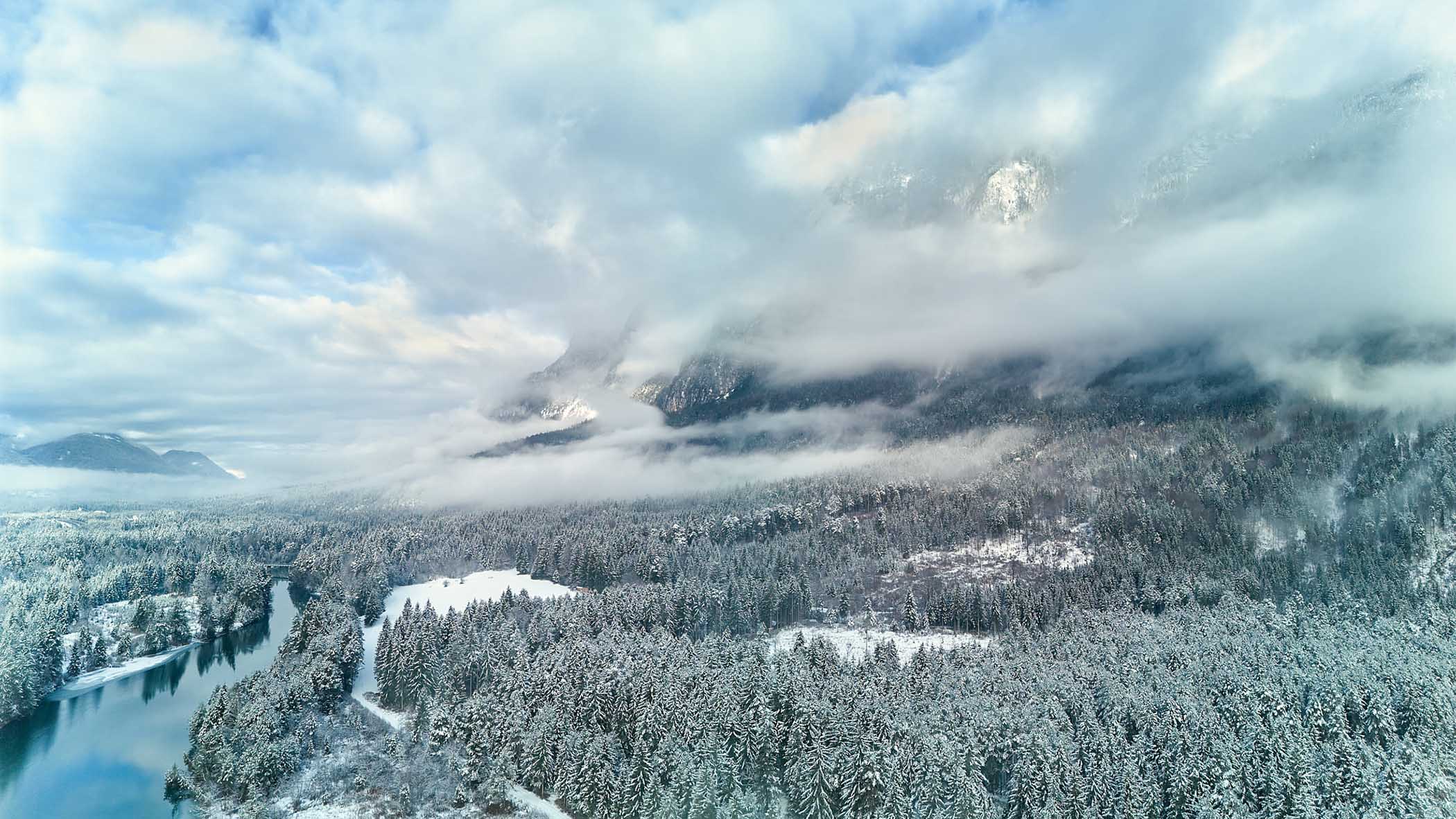 Winterliche Landschaft im Naturpark Schütt mit verschneiten Wäldern, ruhigem Fluss und tief hängendem Nebel vor den Bergen – fotografiert von Atelier Schulte.