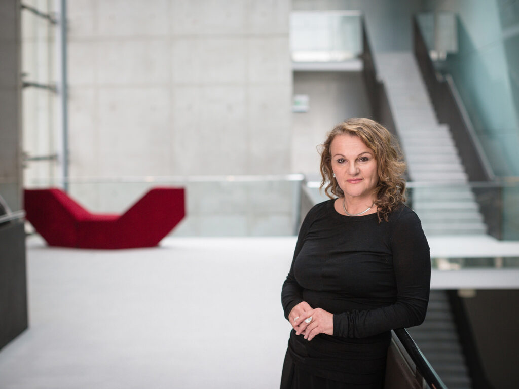 Businessportrait einer Frau in einem modernen architektonischen Innenraum mit klaren Linien und offener Raumstruktur.