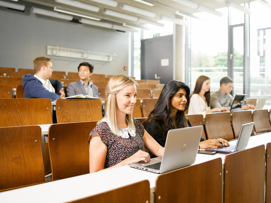Studierende arbeiten mit Laptops in einem modernen Seminarraum mit natürlichem Licht.