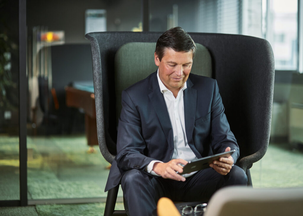 Businessportrait eines Mitarbeiters im modernen Arbeitsumfeld, vertieft in die Arbeit am Tablet – Beispiel für authentische Mitarbeiterfotos und typische Kostenfaktoren im Unternehmenskontext.