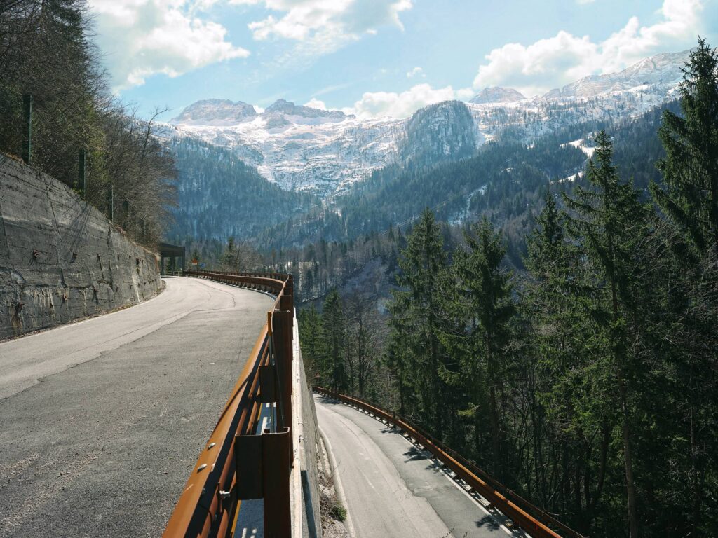 Bergstraße mit Leitplanke und doppelter Linienführung in alpiner Landschaft mit Blick auf bewaldetes Tal und Berge