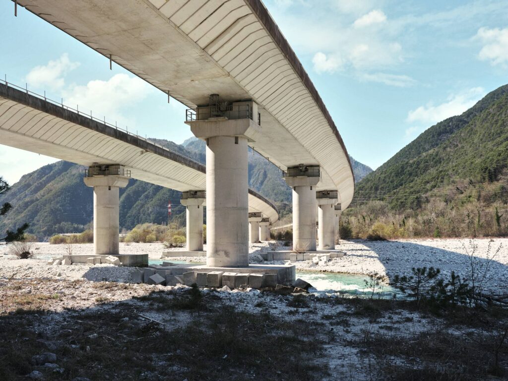 Brücke auf Pfeilern als strukturierendes Element in einer alpinen Landschaft mit Flussbett