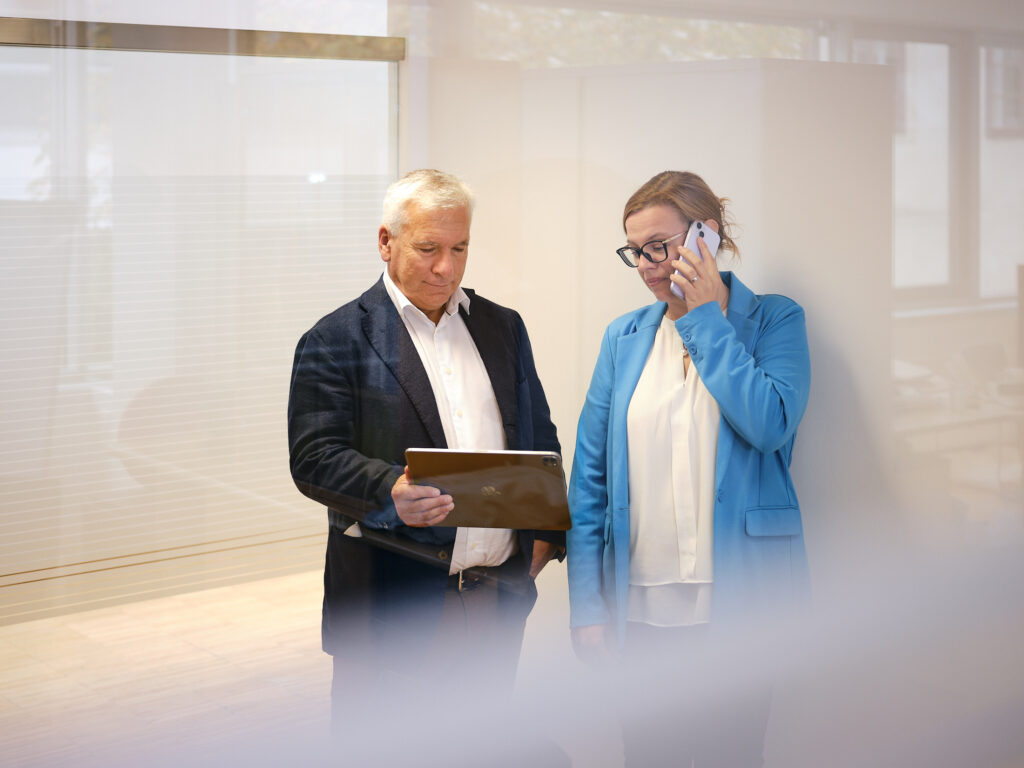 Businessmeeting im Büro: Zwei Mitarbeitende besprechen Unterlagen am Tablet, während eine Kollegin telefoniert – professionelle Businessfotografie von Atelier Schulte für Unternehmenskommunikation in Österreich.