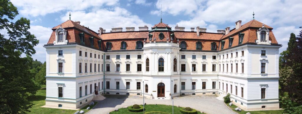 Drohnenaufnahme eines historischen Schlosses mit symmetrischer Architektur und ruhigem Licht, eingebettet in eine weitläufige Parklandschaft.