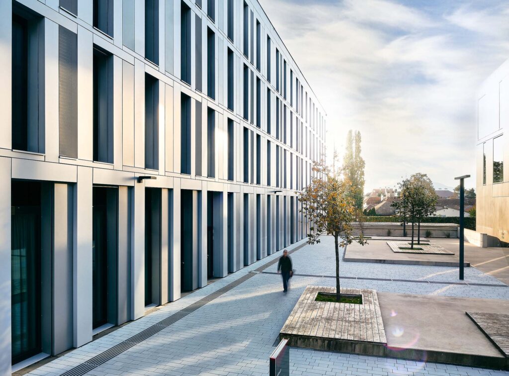 Moderner Innenhof mit klar strukturierten Fassaden, ruhigem Seitenlicht und einer Person in Bewegung, fotografiert im urbanen Stadtraum.