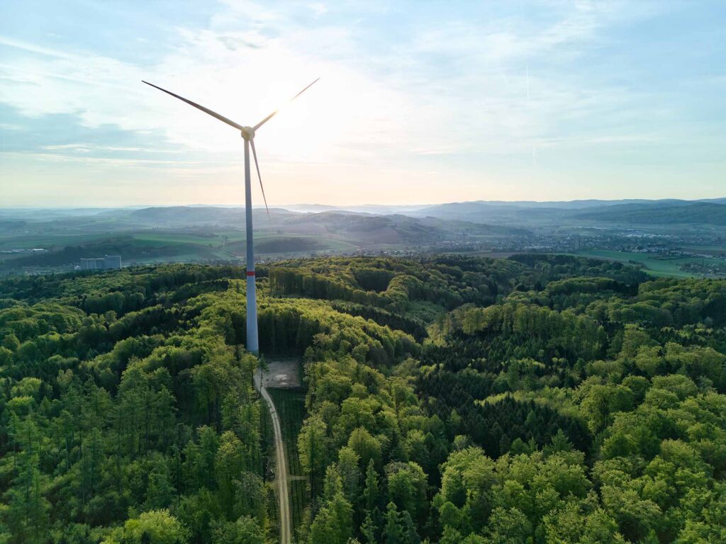 Professionelle Drohnenfotografie in Österreich mit Windkraftanlage über bewaldeter Landschaft im Abendlicht – atmosphärische Aerial-Aufnahme von Atelier Schulte für Architektur, Energieunternehmen und moderne Unternehmenskommunikation im Alpen-Adria-Raum.